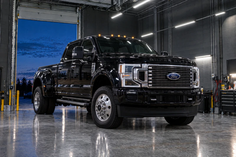 A black Ford F-450 Super Duty dually pickup parked in a clean service bay, roll-up door open at dusk